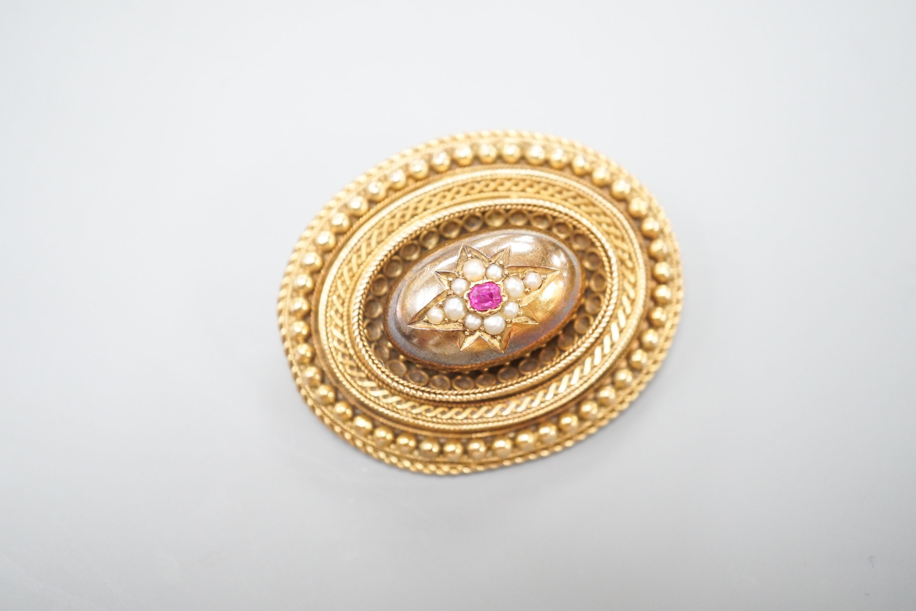 A Victorian yellow metal, ruby? and seed pearl set oval brooch, with glazed back, 43mm, gross weight 18.7 grams.